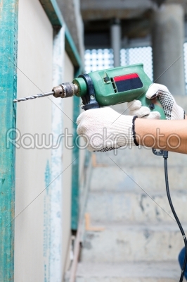 worker drilling with machine in construction site wall