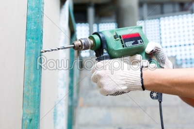 worker drilling with machine in construction site wall