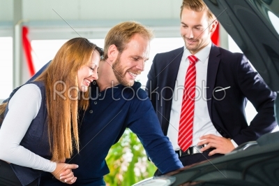 Young Couple and seller with auto in car dealership
