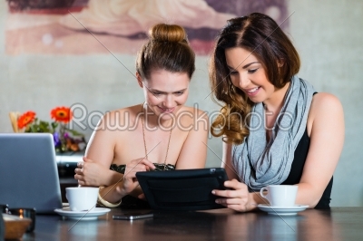 Young women or colleagues sitting in a cafe or restaurant, and looking on the Tablet Computer