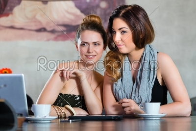 Young women or colleagues sitting in a cafe or restaurant, and looking on the Tablet Computer