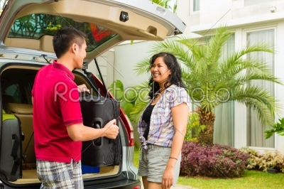 Asian couple packing car with suitcases for holiday
