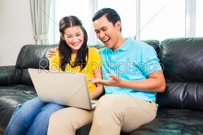 Asian couple using laptop on sofa