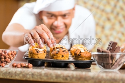 Asian man baking muffins in home kitchen