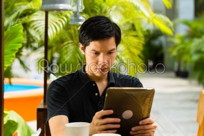 Asian man is sitting in a bar or cafe outdoor