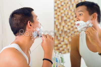 Asian man shaving in front of mirror