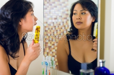 Asian woman combing hair in bathroom mirror