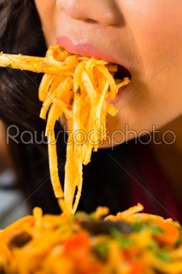 Asian woman eating pasta with chopsticks