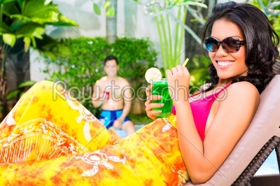 Asian woman tanning at pool with cocktail