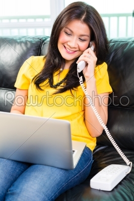 Asian woman using laptop and phone on couch