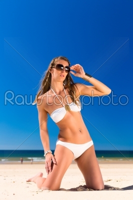 Attractive Woman in white bikini sitting in the sun on beach, a lot of copyspace in the blue sky
