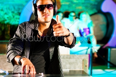 Black DJ in a club at the turntable, in the background the crowd is cheering