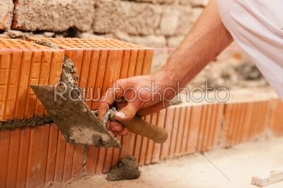 bricklayer making wall with brick and grout