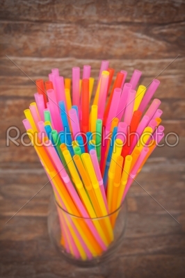 colorful plastic straws in glass on brick background
