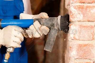 Construction worker removing the plaster from a brick wall in the course of a renovation or restoration of a building