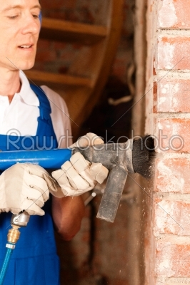 Construction worker removing the plaster from a brick wall in the course of a renovation or restoration of a building