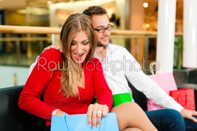 Couple - man and woman - in a shopping mall with colorful bags looking at their bought stuff