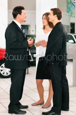 Couple with salesman at car dealer 