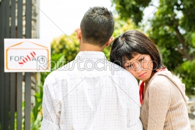 disappointed asian couple in front of a house