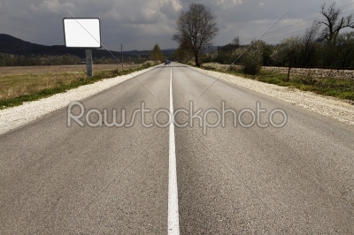 empty road through fields with blank billboard beside   