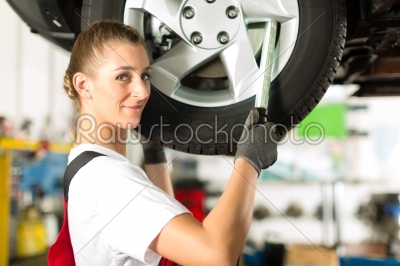 Female car mechanic working on jacked auto