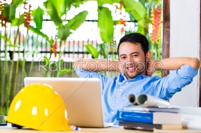 Freelancer - Architect working at home on a design or draft, on his desk are books, a laptop and a helmet or hard hat
