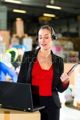 Friendly Woman, dispatcher or supervisor using headset and laptop at warehouse of forwarding company, smiling