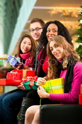 Friends with Christmas presents and bags in mall