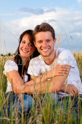 Happy couple sitting on a meadow or grainfield