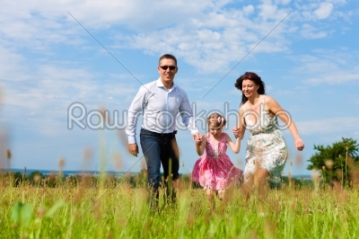 Happy family running on meadow in summer