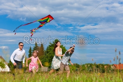 Happy family running on meadow with a kite