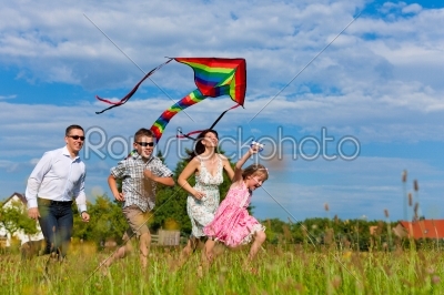 Happy family running on meadow with a kite