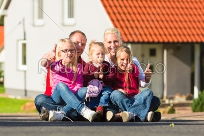 Happy family sitting in front of home