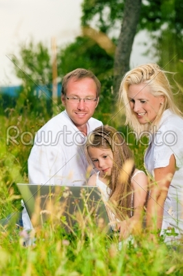 Happy family sitting in meadow with Laptop Computer