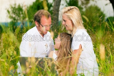 Happy family sitting in meadow with Laptop Computer