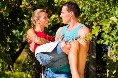 Man carries woman on his arms in vineyard