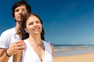 Playful couple on the ocean beach enjoying their summer vacation, he embraces her