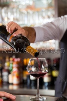Red wine pouring in glass at bar