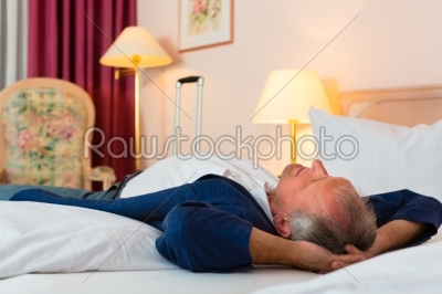 Senior man lying on the bed in the hotel room