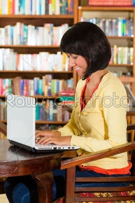 Student - Young woman in a library, writes on laptop learning