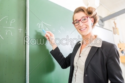 Teacher writing with chalk in front of school class on board