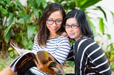 Two Asian girlfriends reading magazine