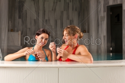 Two female friends drinking tea in swimming pool