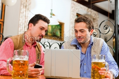 Two friends in Bavarian pub with laptop