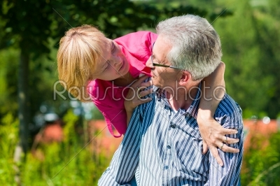 Visibly happy mature or senior couple outdoors arm in arm, he is carrying her piggyback