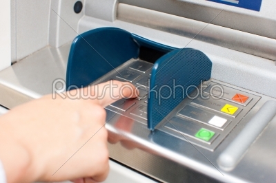 Woman at ATM or cash dispenser and is entering her PIN
