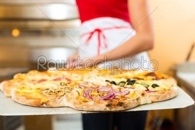 Woman pushing the finished pizza from the oven