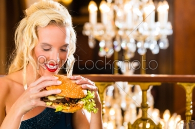 Young woman in fine restaurant, she eats a burger