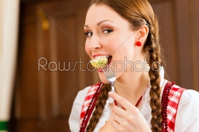 Young woman in traditional Bavarian Tracht eats in restaurant or pub