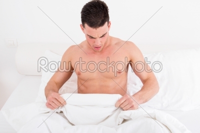  half naked young man in bed  looking down at his underwear